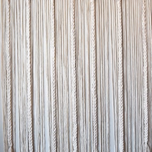 May include: A white macrame wall hanging with a scalloped top and long, braided strands.