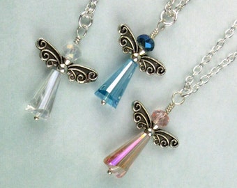 May include: Three angel-shaped pendants on silver-tone chains. Each pendant features a faceted crystal body in clear, light blue, or light pink, topped with a round crystal bead and silver-tone metal wings with a swirling filigree design.