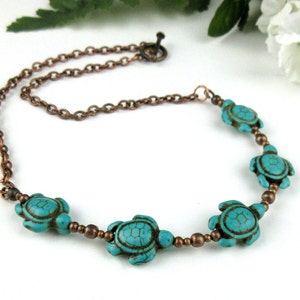 May include: A turquoise blue necklace with five turtle charms and a copper chain. The necklace is made with small copper beads between the turtle charms.