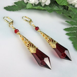 May include: A pair of long, dangling earrings with gold filigree and a deep red crystal teardrop. The earrings have a vintage style.