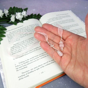 May include: Two handmade bookmarks with pink rose quartz beads and silver-tone accents. Each bookmark has a sheer pink ribbon for easy placement in a book. The bookmarks are displayed open on a book.