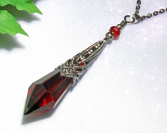 May include: A silver chain necklace with a red crystal pendant. The pendant is shaped like a teardrop and has a detailed silver filigree design.