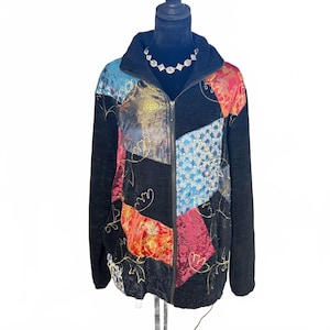 May include: A black zip-up jacket featuring a patchwork design of textured black fabric and colorful panels in red, blue, and gold with intricate floral and geometric patterns. The jacket has a high collar and long sleeves with gold embroidery.