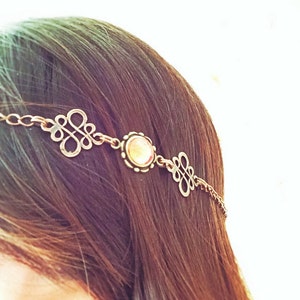 May include: A gold chain headband with a clear gemstone and two decorative knots. The headband is worn on a person's head.