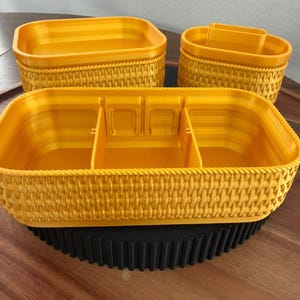 May include: Three yellow plastic storage containers with a textured woven pattern on the exterior sides. The largest container is rectangular with internal dividers, while the two smaller containers are oval and rectangular.