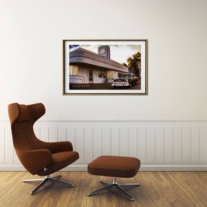 May include: A vintage black car parked in front of a retro diner with a red and white sign that says "Diner". The diner has a white facade with large windows and a flat roof. The image is in a framed print.