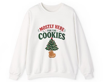 May include: A white long-sleeve crewneck sweatshirt featuring the red and green text "MOSTLY HERE FOR THE COOKIES" above a graphic of a decorated Christmas tree and a single brown gingerbread cookie shaped like a tree ornament.