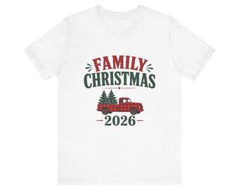May include: A white short-sleeve t-shirt featuring a graphic print with the red text FAMILY and green text CHRISTMAS above a red plaid pickup truck carrying two green pine trees, with the year 2026 printed in green below the truck.