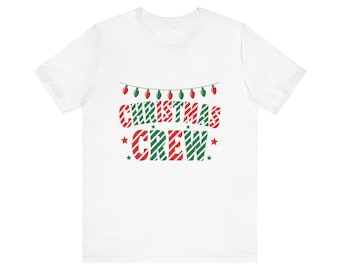 Peut inclure: Un t-shirt blanc à manches courtes avec une impression graphique représentant une guirlande de lumières de Noël rouges et vertes au-dessus du texte CHRISTMAS CREW en rayures diagonales rouges et vertes, avec de petites étoiles vertes.