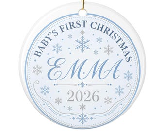 May include: A round white ceramic Christmas ornament featuring a light blue border and snowflake patterns. The text reads Baby's First Christmas, the name Emma in a large script font, and the year 2026. A gold string is attached at the top.