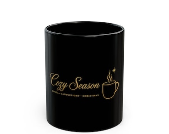 May include: A black ceramic mug featuring gold text that reads Cozy Season, with the words COCOA, CANDLELIGHT, CHRISTMAS printed below. A gold graphic of a steaming mug and a small star is positioned to the right of the text.
