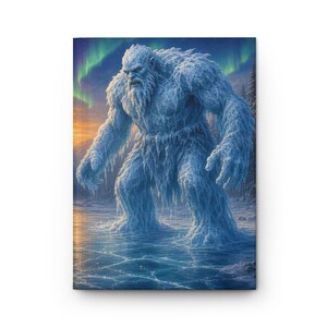 May include: A hardcover journal featuring a graphic illustration of a large, white, fur-covered yeti standing on a frozen, cracked lake surface. The background displays a vibrant green aurora borealis in the night sky above a dark forest.