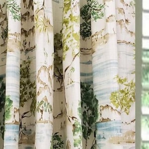 May include: Cream-colored curtains with a watercolor landscape design. The curtains feature a repeating pattern of trees, hills, and water in shades of green, brown, and blue. The fabric is slightly textured.