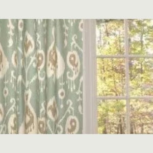 May include: A pair of teal blue curtains with a white and brown ikat pattern. The curtains are hung in front of a window with a view of trees.
