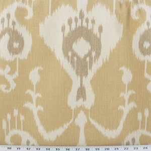 May include: Close-up of a fabric with a repeating ikat pattern. The design features large, stylized shapes in off-white and taupe against a golden-yellow background. The fabric has a textured appearance, suitable for upholstery or home decor.