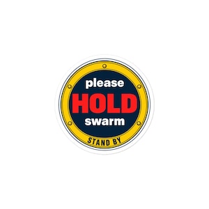 May include: A circular sticker with a dark blue centre and a yellow border featuring four small gold rivets. The text reads please HOLD swarm in white and red, with the words STAND BY printed in black at the bottom of the yellow border.