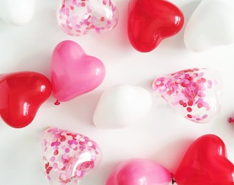 Puede incluir: Una colección de globos en forma de corazón de varios colores, incluyendo rojo, rosa y blanco. Algunos globos tienen confeti dentro.