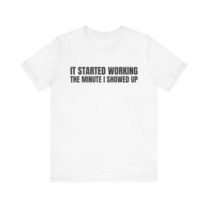 May include: A white short-sleeved t-shirt featuring the black text IT STARTED WORKING THE MINUTE I SHOWED UP printed in a bold, sans-serif font across the center of the chest. The garment has a crew neckline and a standard fit.
