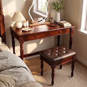 May include: A dark wood vanity desk with two drawers and turned legs, accompanied by a matching tufted dark brown leather stool. The desk features an irregular-shaped LED mirror, a pleated lamp, a white vase with greenery, and books.