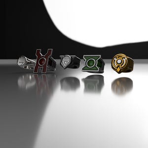 May include: A collection of five metal rings featuring distinct emblems. The rings include a silver circular design, a tall red and black symbol, a black shield-shaped icon, a green square emblem, and a gold circular logo with a central cutout.