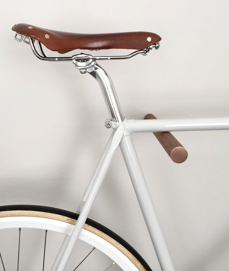 This pair of wooden bike hooks comes in black walnut wood with a front in copper. The wall mounted hooks hold a minimalistic sports bike in light grey. Only recommended for bicycles up to 13 kg.