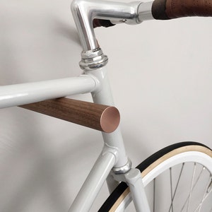 This pair of wooden bike hooks comes in black walnut wood with a front in copper. The wall mounted hooks hold a minimalistic sports bike in light grey. Only recommended for bicycles up to 13 kg.