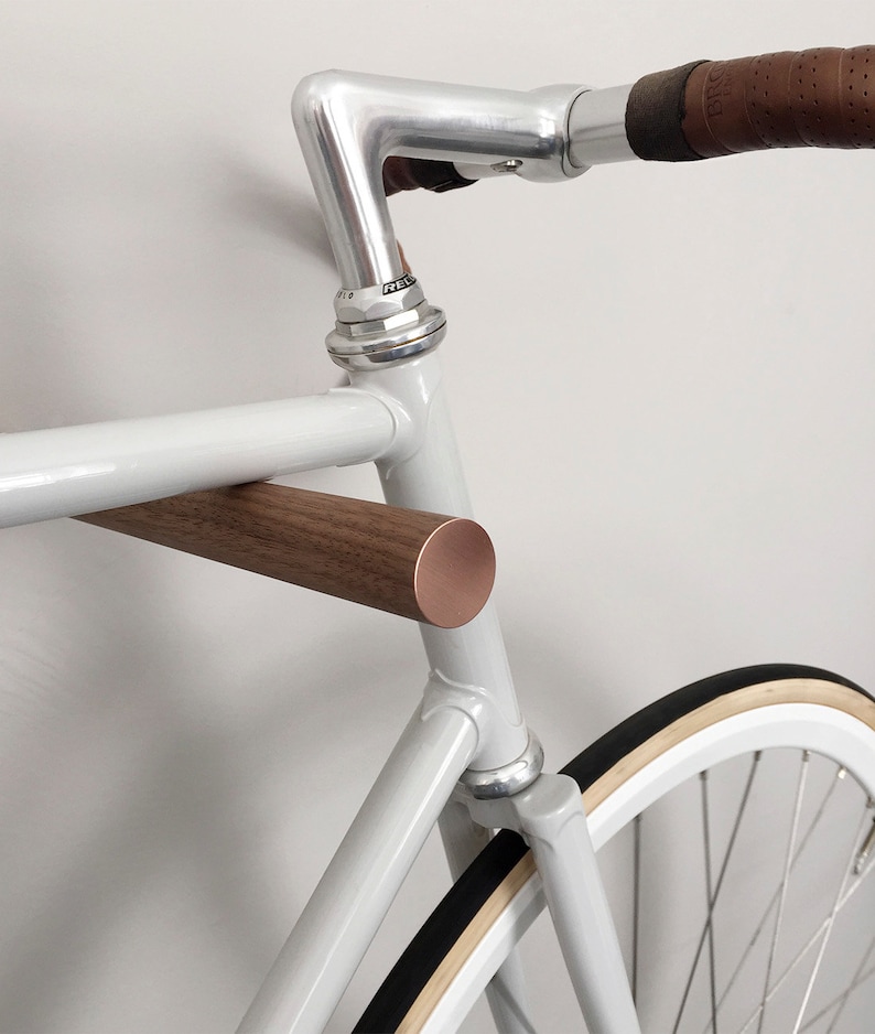 This pair of wooden bike hooks comes in black walnut wood with a front in copper. The wall mounted hooks hold a minimalistic sports bike in light grey. Only recommended for bicycles up to 13 kg.