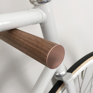 This pair of wooden bike hooks comes in black walnut wood with a front in copper. The wall mounted hooks hold a minimalistic sports bike in light grey. Only recommended for bicycles up to 13 kg.