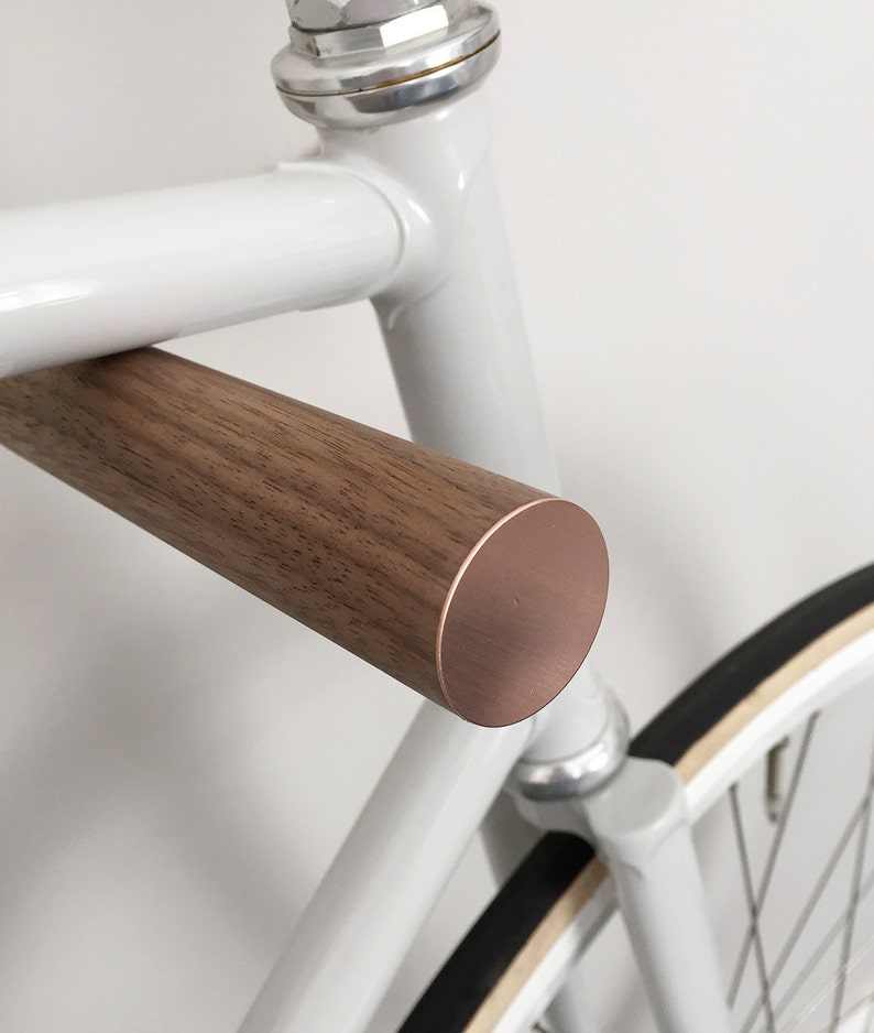 This pair of wooden bike hooks comes in black walnut wood with a front in copper. The wall mounted hooks hold a minimalistic sports bike in light grey. Only recommended for bicycles up to 13 kg.