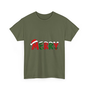 Può includere: Una t-shirt a maniche corte color verde oliva con la scritta MERRY in lettere rosse e verdi. La lettera M è sormontata da un cappello da Babbo Natale rosso, la E presenta delle lucine e la Y è decorata con bacche di agrifoglio rosse.