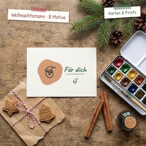 May include: A white rectangular greeting card featuring a tan organic shape with a black line drawing of a Santa Claus face, the text "Für dich," and a small elf icon. The card is displayed with a watercolor set, cinnamon sticks, and cookies.