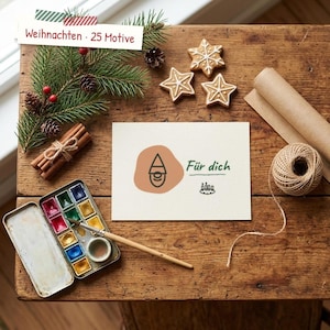 May include: A rectangular card featuring a gnome illustration on a peach-colored circle, the text "Für dich," and a small candle wreath icon. The card is surrounded by pine branches, star-shaped cookies, cinnamon sticks, and a watercolor set.