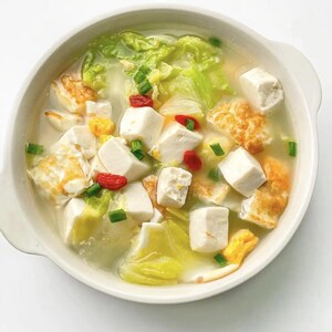 Puede incluir: Un cuenco blanco lleno de un caldo claro que contiene cubos de tofu blanco, trozos de huevo frito dorado, hojas de col verde brillante y pequeñas bayas de goji rojas, adornado con cebolletas verdes picadas por toda la sopa.