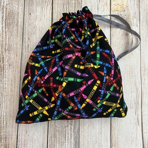 Pode incluir: Uma bolsa de cord&atilde;o preto com um padr&atilde;o de giz de cera colorido. Os giz de cera est&atilde;o dispostos em diagonal e t&ecirc;m as palavras "vermelho", "azul", "amarelo", "verde", "roxo", "laranja" e "rosa" escritas neles.