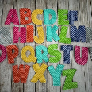 Pode incluir: Um conjunto de letras do alfabeto de feltro em v&aacute;rias cores com um padr&atilde;o de diamante. As letras est&atilde;o dispostas em ordem alfab&eacute;tica sobre um fundo de madeira.