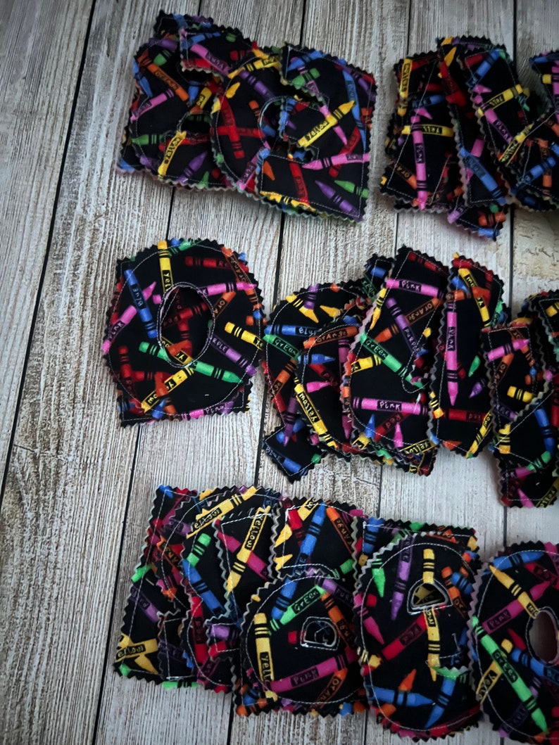 Pode incluir: Um conjunto de letras do alfabeto de feltro com um design de impress&atilde;o de giz de cera. As letras s&atilde;o pretas com desenhos de giz de cera coloridos. As letras s&atilde;o todas mai&uacute;sculas e est&atilde;o dispostas em uma ordem aleat&oacute;ria.