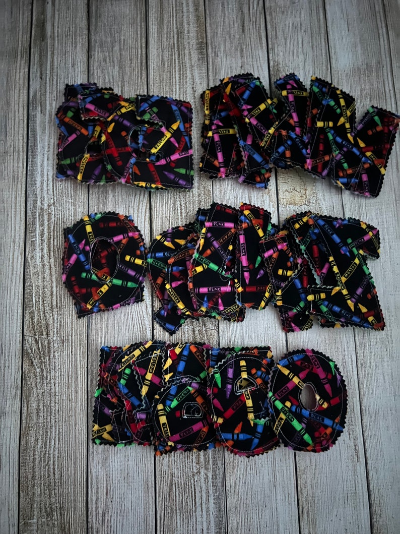 Pode incluir: Um conjunto de letras de feltro que soletram a palavra "READ" com um padr&atilde;o de giz de cera. As letras s&atilde;o pretas com desenhos de giz de cera coloridos.