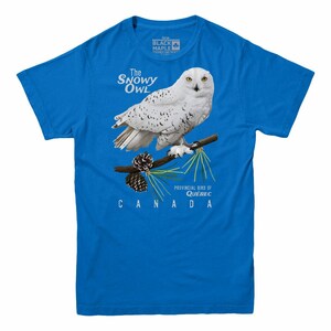 May include: A blue t-shirt with a white snowy owl perched on a branch with pine cones. The text "The Snowy Owl" is above the owl and "Provincial Bird of Quebec CANADA" is below the owl.