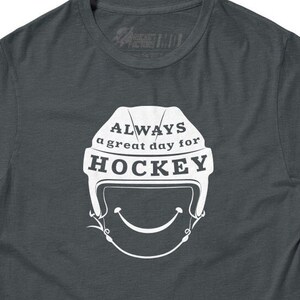 May include: A dark gray t-shirt with a white graphic of a hockey helmet with a smiling face and the text "ALWAYS a great day for HOCKEY".