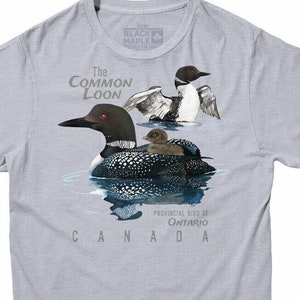 May include: A light grey t-shirt with a graphic of a common loon, its chick, and a reflection of the loon in the water. The text "The Common Loon" is above the loon and "Provincial Bird of Ontario CANADA" is below the loon.