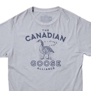 May include: A light gray t-shirt with a blue graphic print of a Canadian goose with the text "The Canadian Goose Alliance".