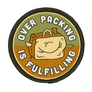 Peut inclure: Un écusson rond brodé de couleur verte et marron avec le texte "Over Packing Is Fulfilling" et une image de dessin animé d'une valise souriante et surchargée.