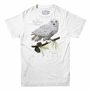 May include: White t-shirt with a snowy owl illustration. The owl is perched on a branch with pine needles and a pine cone. The text "The Snowy Owl" is above the owl and "Provincial Bird of Quebec CANADA" is below the owl.