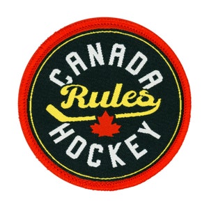 Peut inclure: Un écusson rond à bordure rouge avec un fond noir. Le texte "CANADA RULES HOCKEY" est écrit en lettres blanches et jaunes autour d'une feuille d'érable rouge et d'un bâton de hockey jaune.