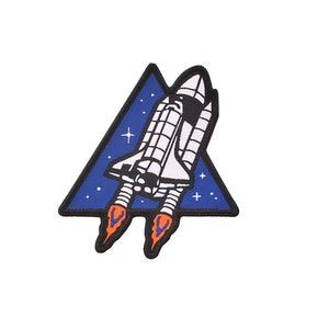 May include: A blue and black triangular patch featuring a white space shuttle taking off. The shuttle has orange flames emanating from the bottom. There are white stars on the blue background.