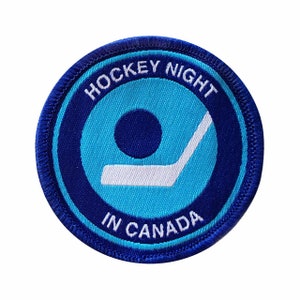 Peut inclure: Écusson brodé bleu et blanc avec le texte "Hockey Night in Canada". L'écusson représente un bâton de hockey et un palet stylisés.
