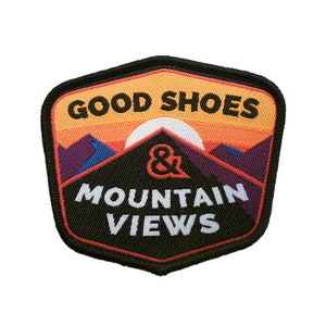 May include: Black and orange embroidered patch with the text "Good Shoes & Mountain Views". The patch features a stylised mountain range with a sun setting behind it.