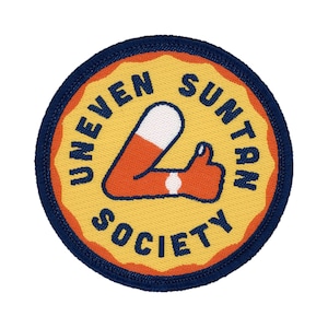 May include: A yellow and orange embroidered patch with a blue border. The patch features a cartoon leg with a tan line and the text "Uneven Suntan Society".