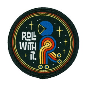 May include: A round, black embroidered patch with a yellow, orange, and red striped figure in a blue helmet. The figure is on a black background with white stars and the text "Roll With It."