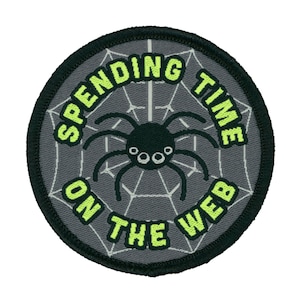 May include: A grey and black embroidered patch with a spider in a web and the text "Spending Time On The Web" in neon green.